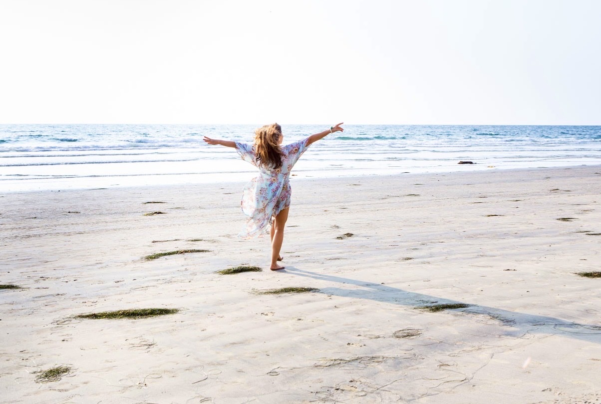 Sienna on the beach with her arms open wide, facing the ocean