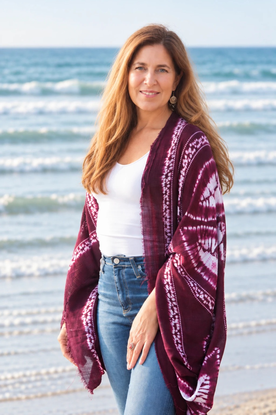 Sienna Smith smiling on the beach in a plum tie-dye wrap, with ocean waves behind her